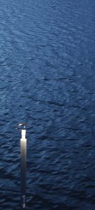 A solitary lamp post standing beside calm, deep blue water, with soft ripples across the surface.
