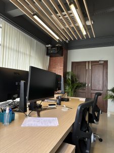 A modern office space with a long wooden desk featuring two black monitors.
