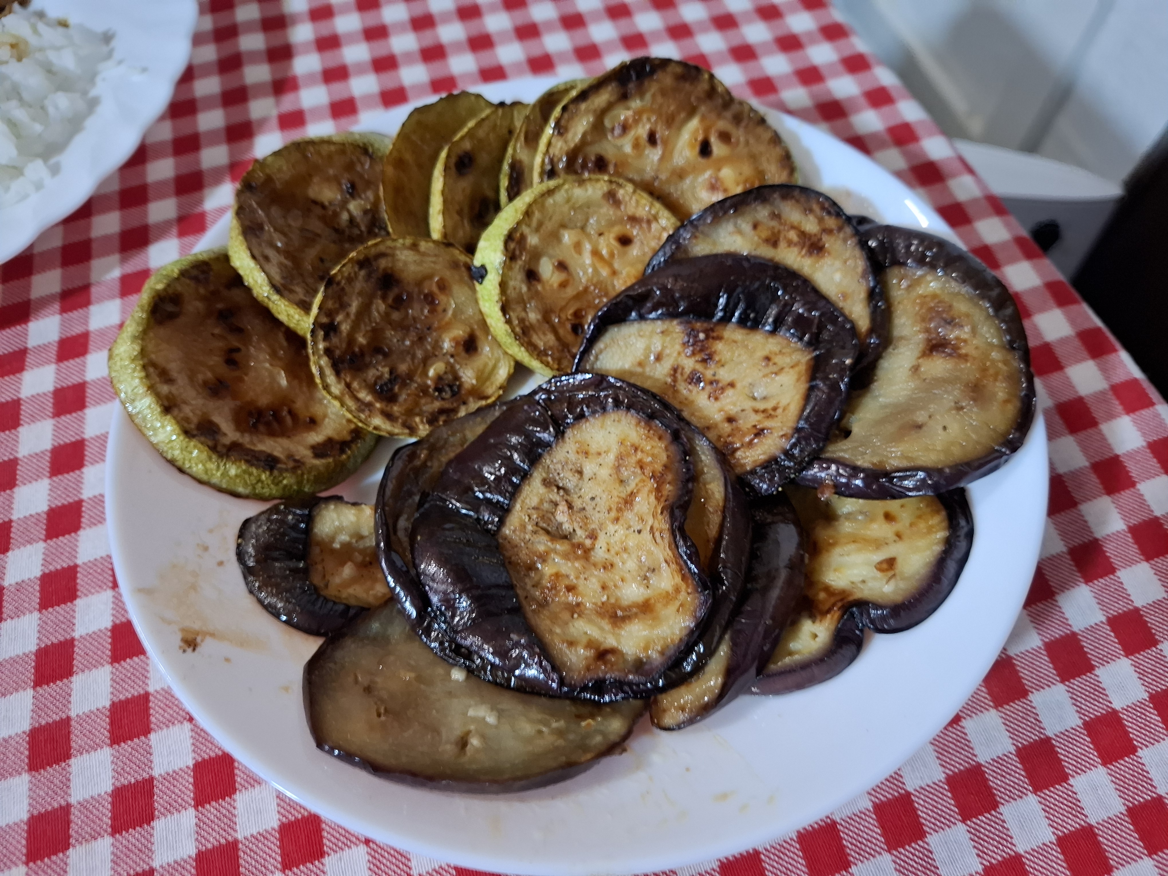Grilled eggplant and zucchini slices sit on a white plate atop a red-and-white tablecloth.
