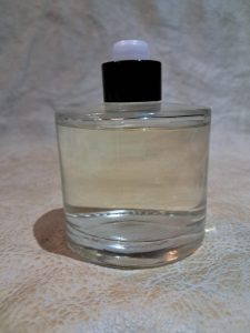 A clear glass bottle partially filled with liquid, featuring a black cap and a white nozzle, placed on a textured beige surface.