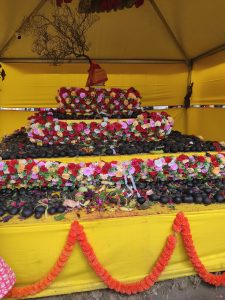 A picture of a hindu god decorated with colorful flowers, cultural stones and wrapped with yellow cloth.
