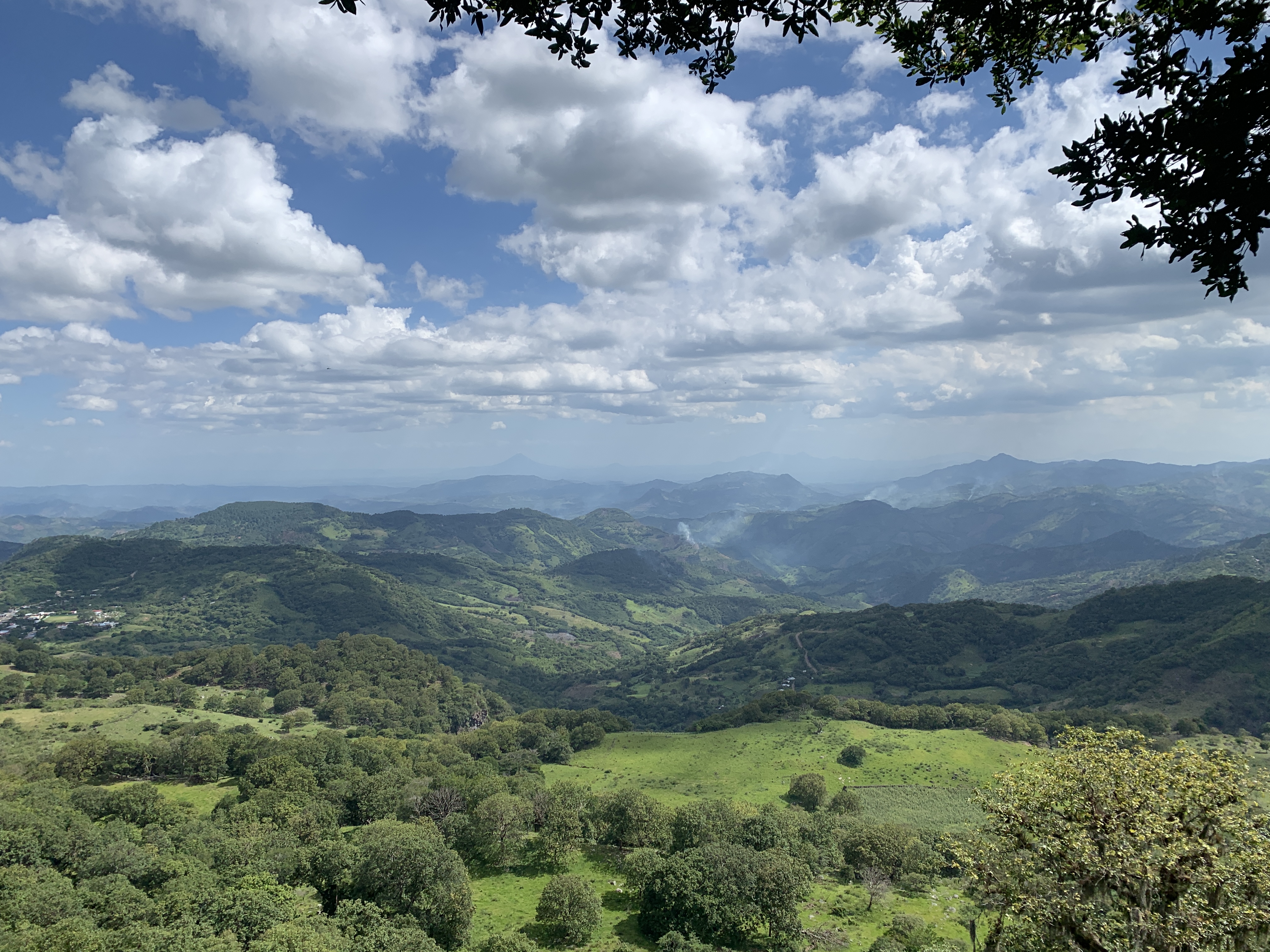 A landscape view of rolling green hills and mountains beneath a partly cloudy sky in Estelí, Nicaragua.