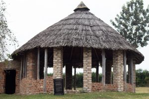 A round traditional hut with a thatched roof, supported by wooden columns and constructed from a combination of mud and brick. 