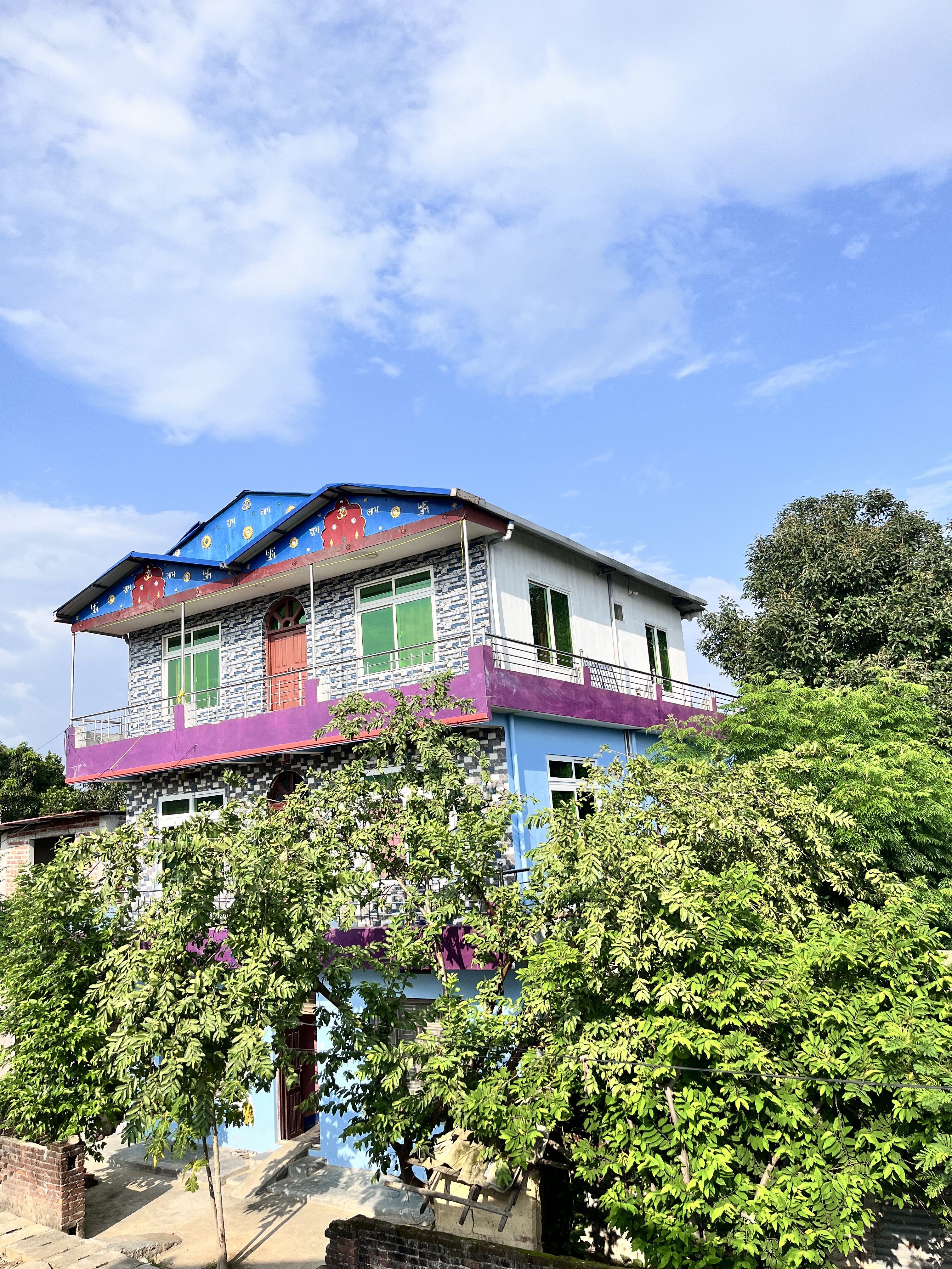 A brightly colored house with a blue roof and decorative patterns rests amidst lush green trees.