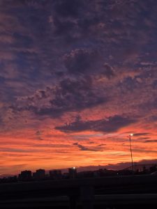 A vibrant sunset fills the sky with shades of orange, pink, and purple, contrasted by dark clouds