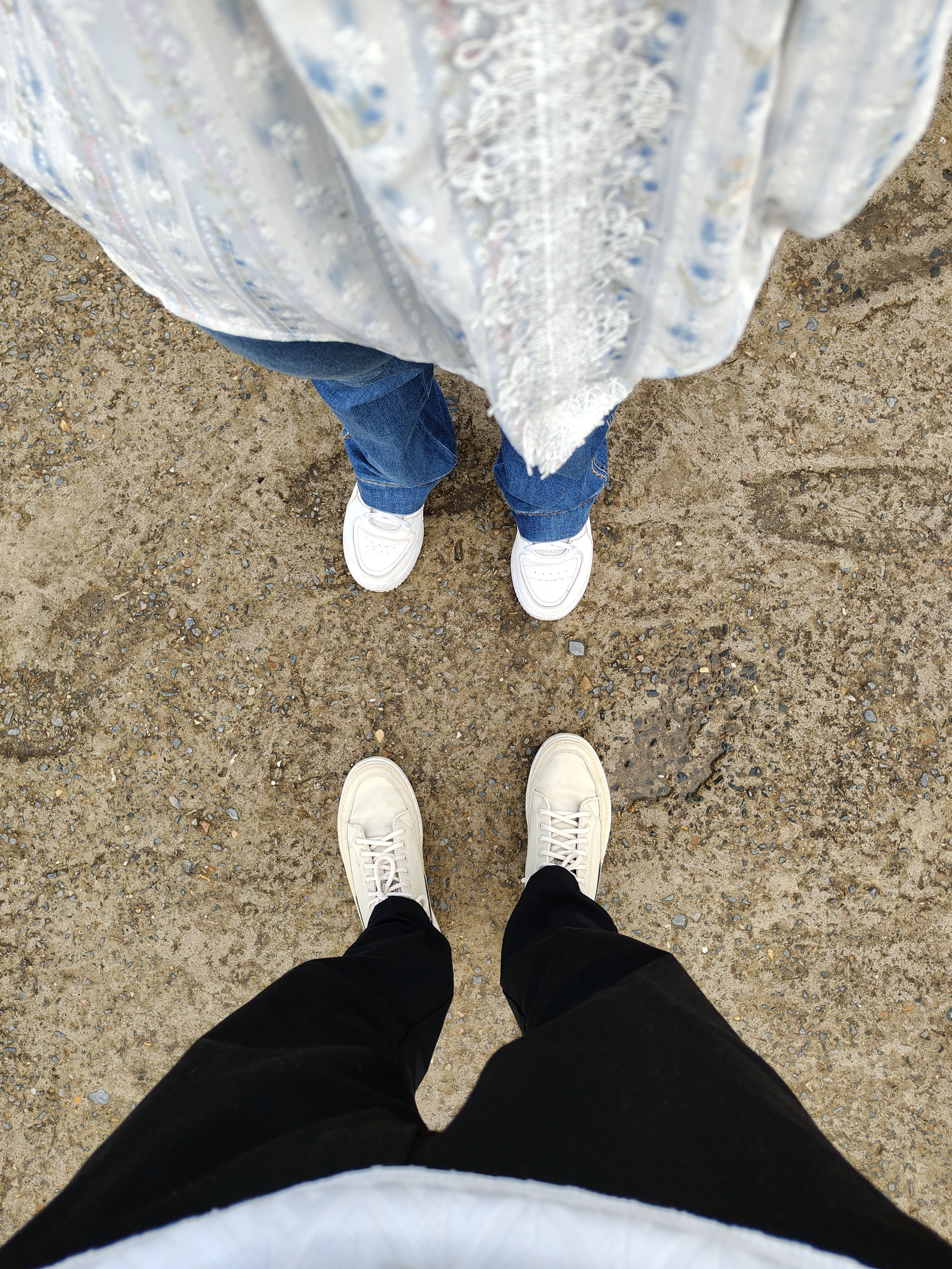The image shows a pair of feet standing on a sandy, gravel surface.