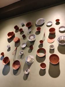 A variety of baking pans and tools are artfully arranged on a textured green wall