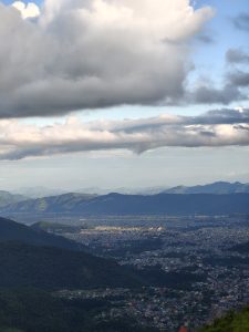 A panoramic view from a high vantage point overlooking a sprawling city nestled in a valley surrounded by mountains.