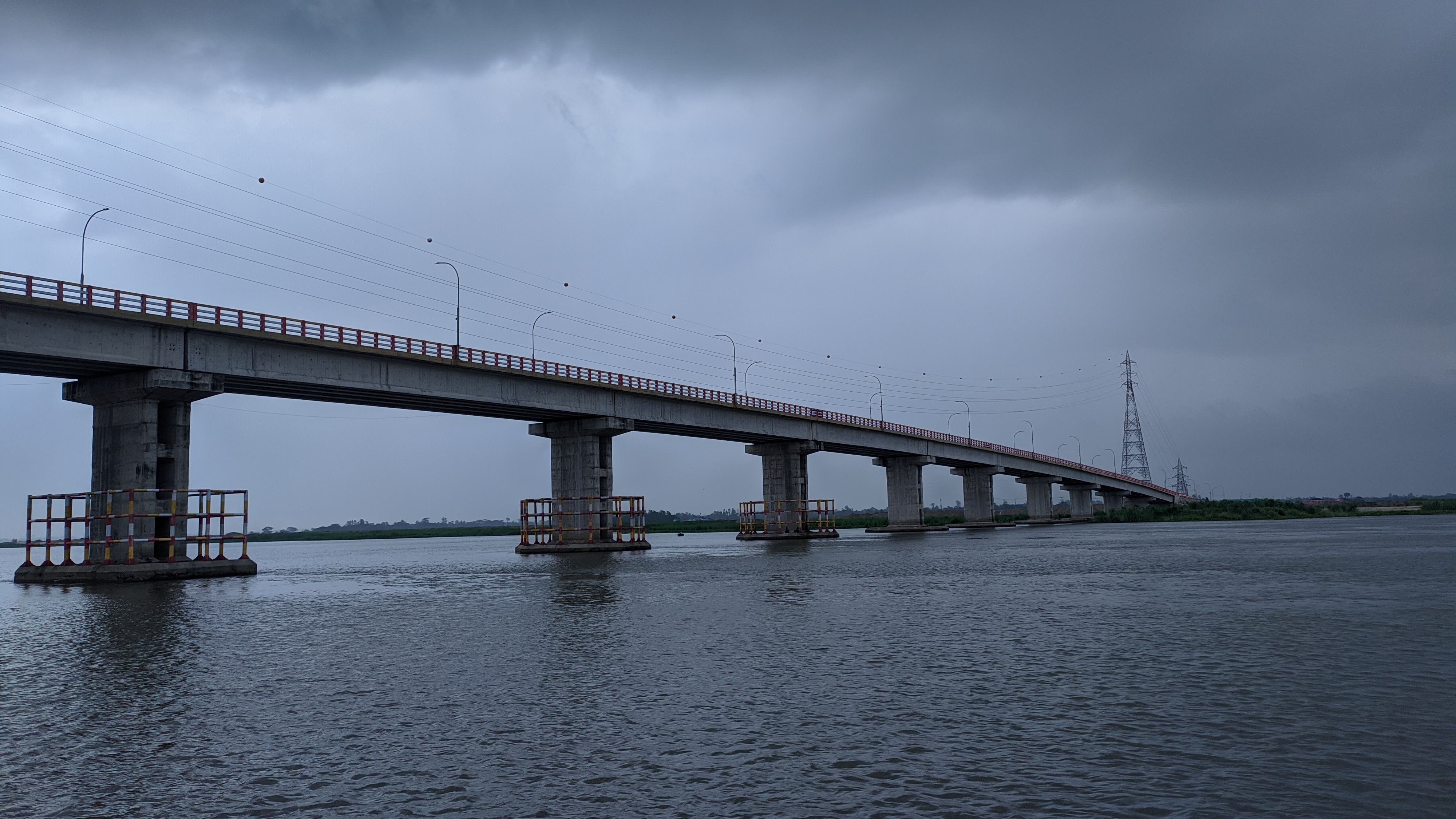 A bridge over a river with two big towers at its end. The sky above it is dark and cloudy.