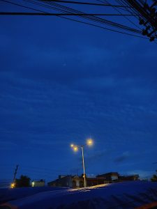 A night scene showing a deep blue sky with scattered clouds and power lines crossing the top of the image.