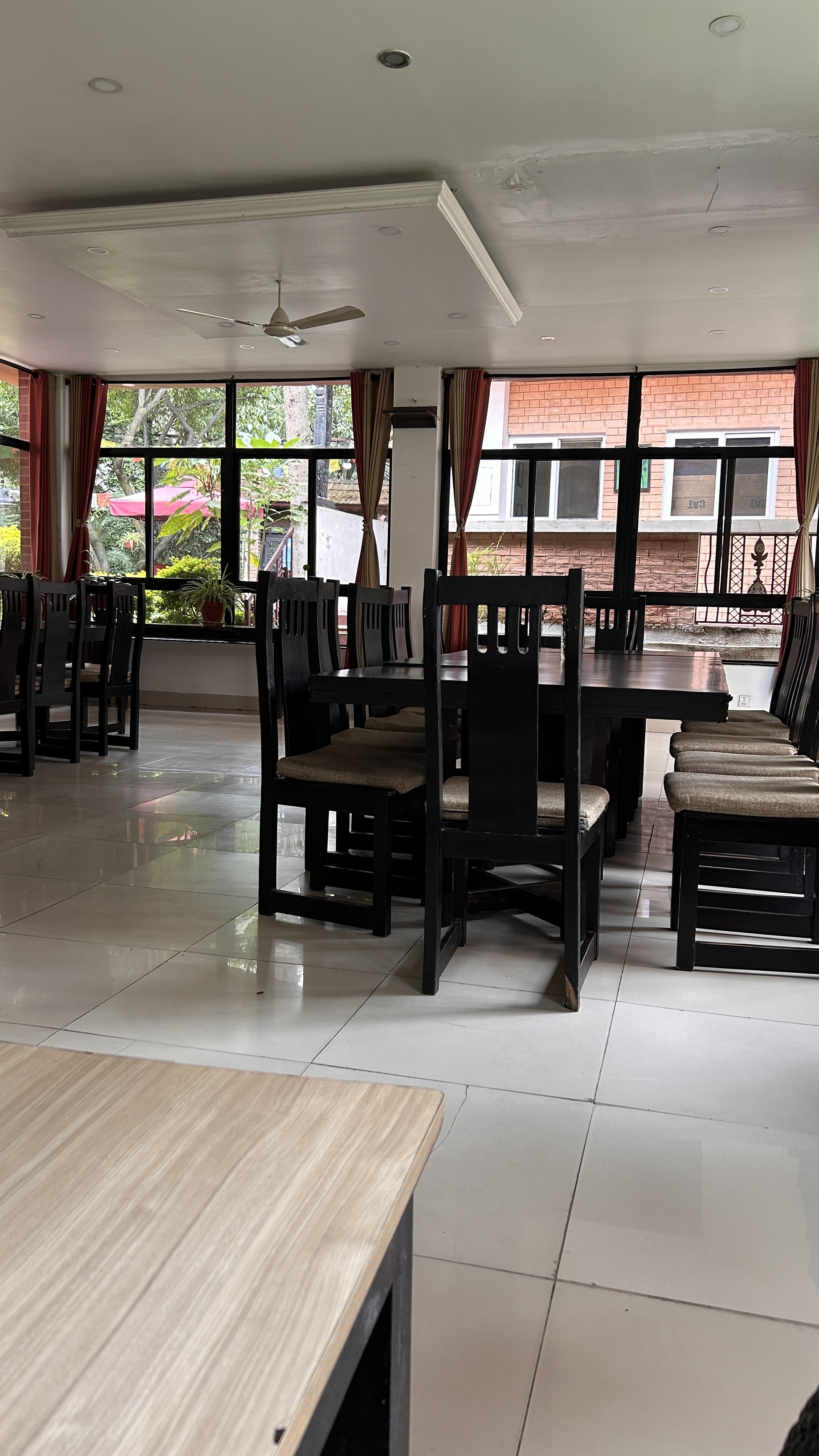 A spacious dining area with a polished white tiled floor, featuring several black wooden tables and chairs.