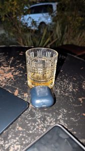 A cold drink in a whiskey glass sits on a sturdy wooden table.