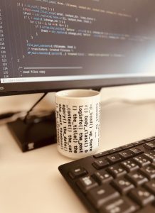 Programing and a teacup (with WordPress code included), monitor screen displays code, code on the tea cup and keyboard.

