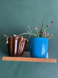 A wooden shelf mounted on a green wall holds two pots. 
