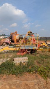 A construction site featuring heavy machinery, including a large concrete mixer partially covered with a tarp and a yellow elevated work platform.