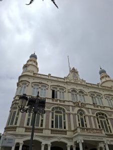 Exterior view of an historic library, featuring ornate neoclassical architecture with arched windows, decorative columns, and domed towers under a cloudy sky.