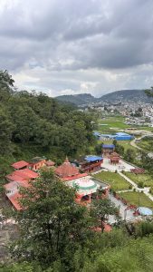 A scenic view of a hilly landscape featuring a cluster of buildings with red rooftops nestled among lush green trees.
