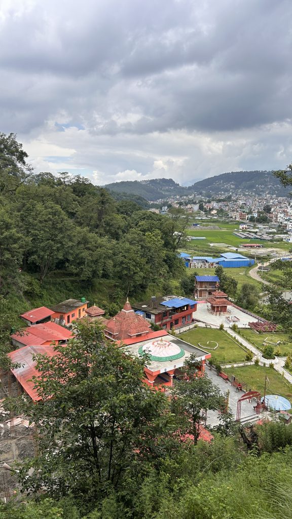 A scenic view of a hilly landscape featuring a cluster of buildings with red rooftops nestled among lush green trees.