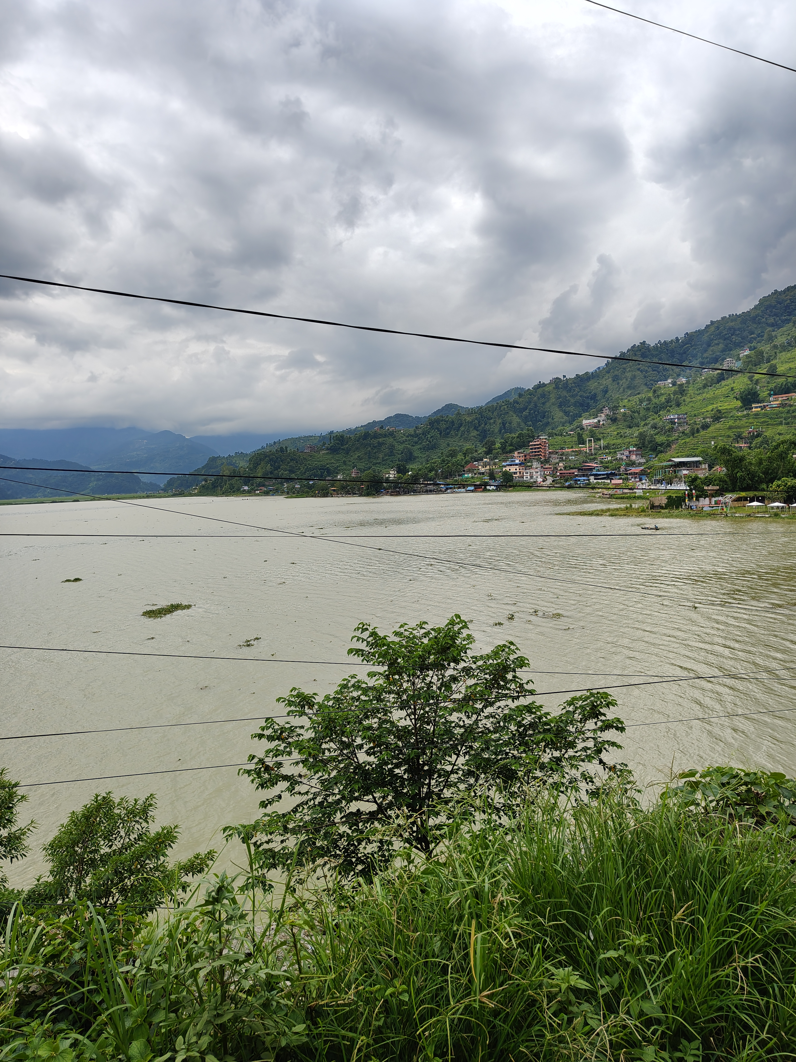A serene lake rests in a lush, green valley, with hills rising in the background under a cloudy sky.
