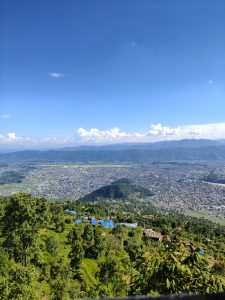 A panoramic view from a high vantage point, showcasing a sprawling landscape beneath a clear blue sky with a few fluffy white clouds. 