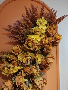 A decorative arrangement of dried flowers featuring orange roses and vibrant yellow blossoms, set against a textured orange backdrop. 