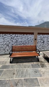A wooden bench with a black metal frame is positioned on a stone patio. 
