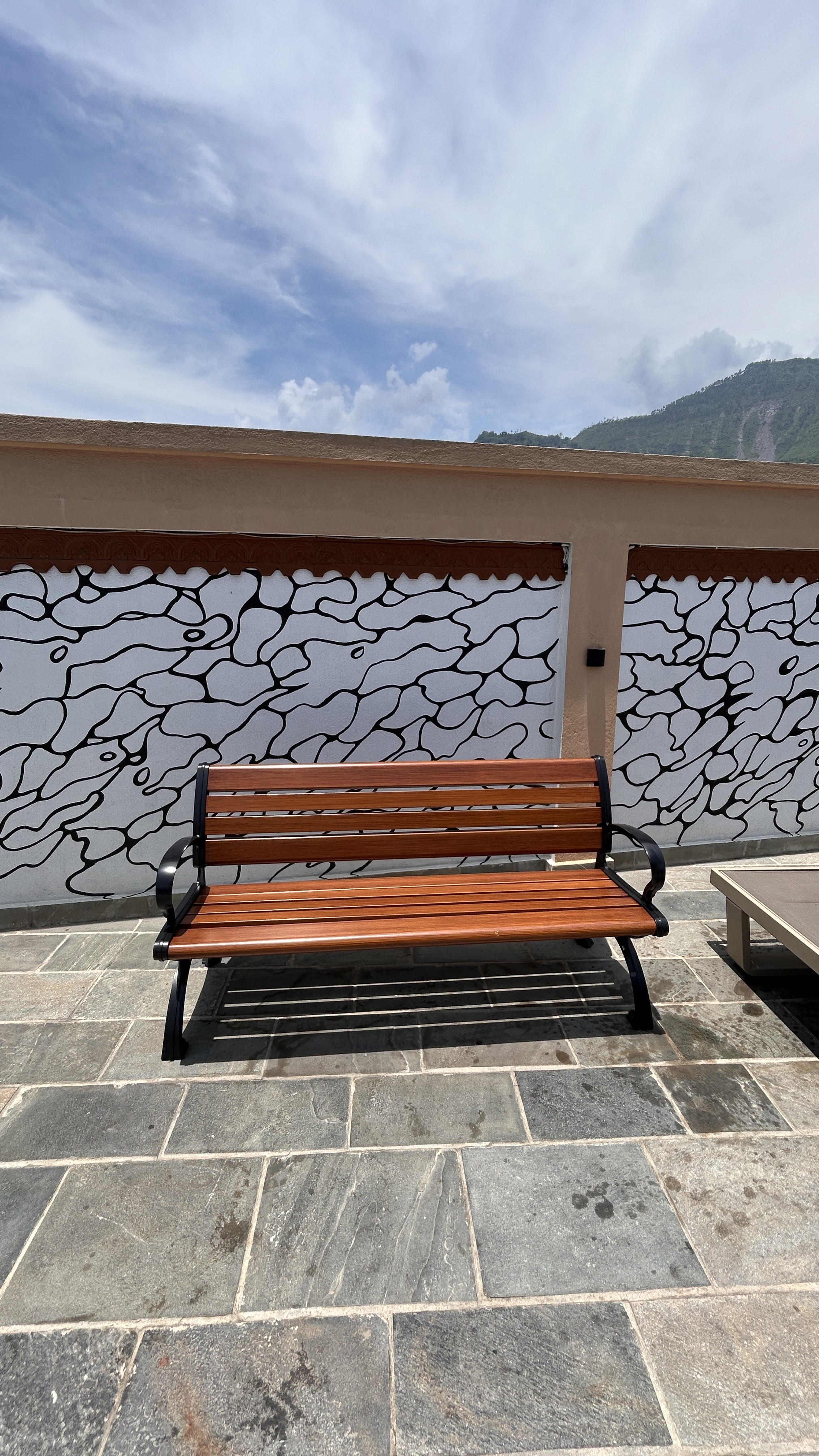 A wooden bench with a black metal frame is positioned on a stone patio.