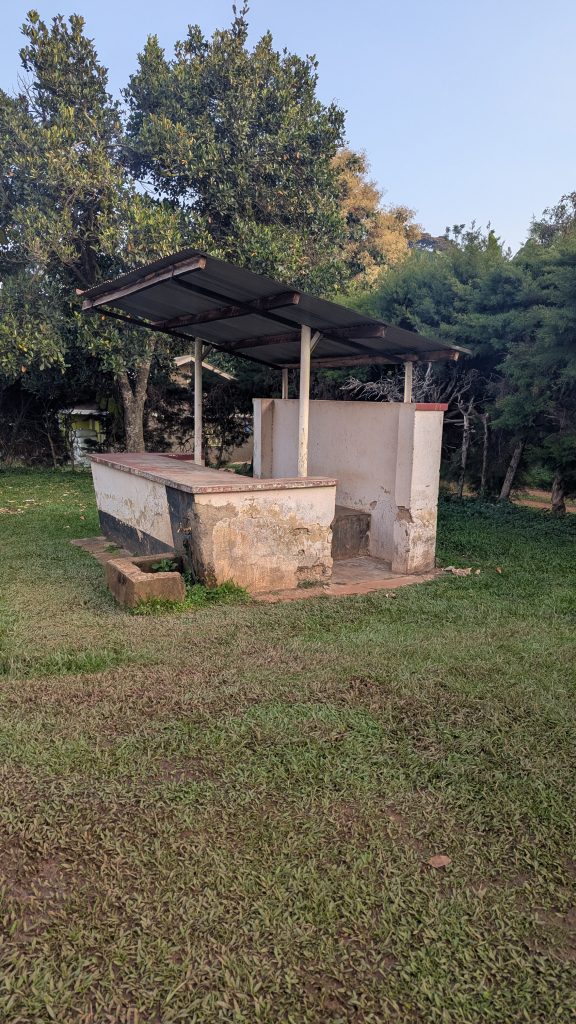 A small, weathered concrete structure with a partial roof stands on a grassy area.