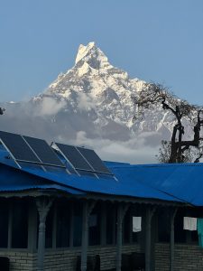 Machhapuchhre mountain range in the distance with clouds glowing orange and yellow in the sunrise.