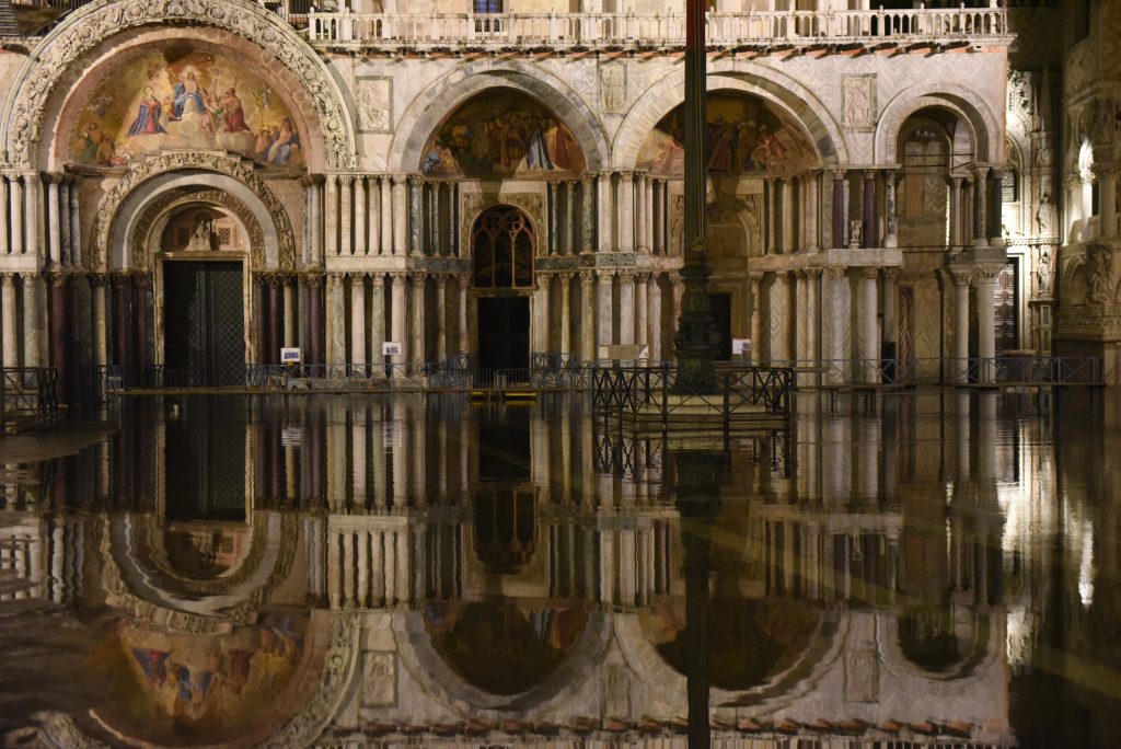 Night view of St. Mark’s Basilica in Venice, Italy, with its ornate arches and mosaics reflected in the flooded square in front of the church