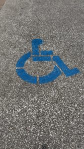Painting of an outline of a person in a wheelchair on pavement, indicating this space is reserved for those with needs.