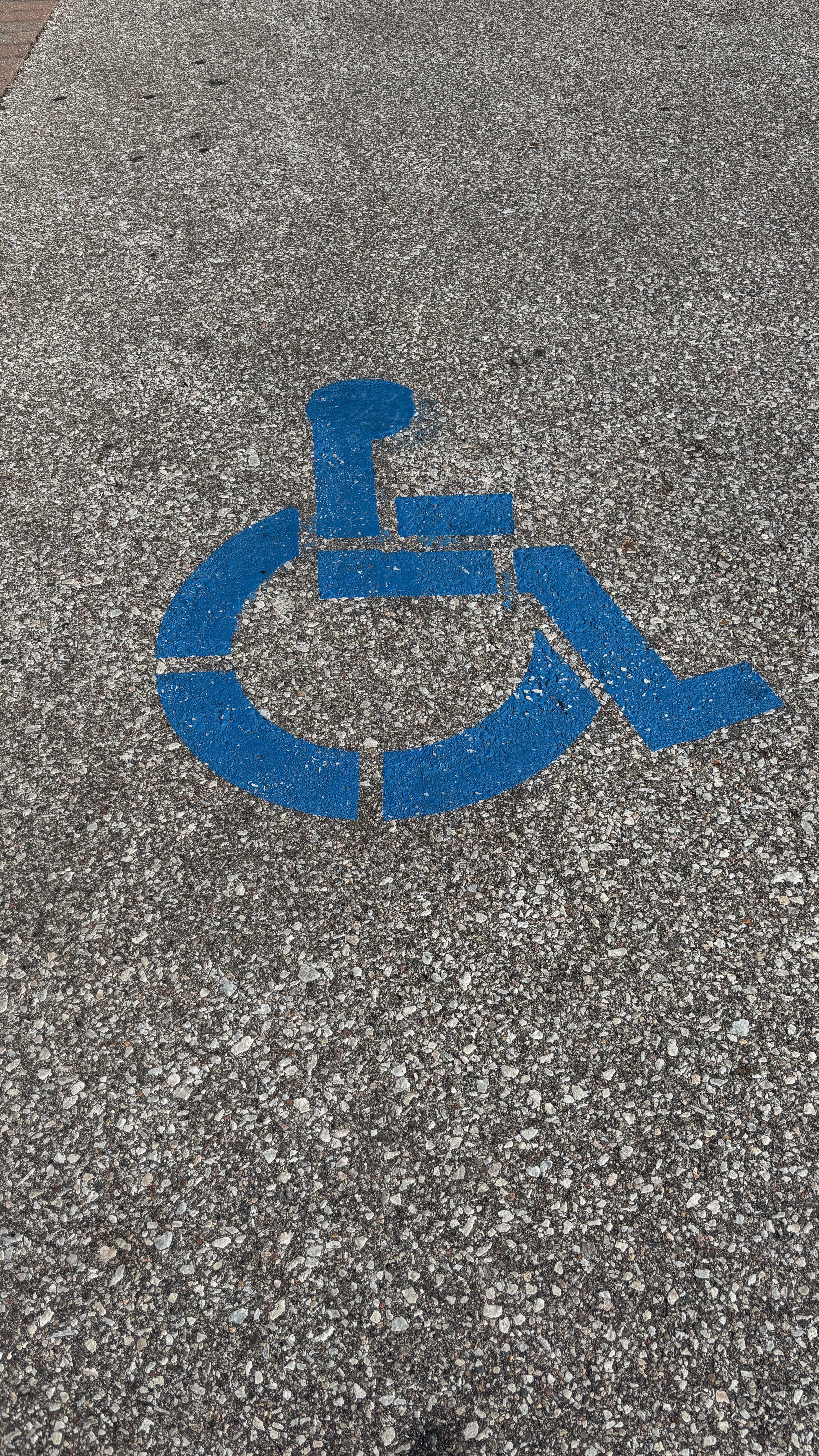 Painting of an outline of a person in a wheelchair on pavement, indicating this space is reserved for those with needs.