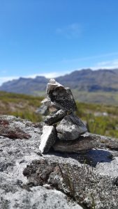 El Cocuy, a delicate stone balance sits atop a rock, set against a deep blue sky and towering mountains.
