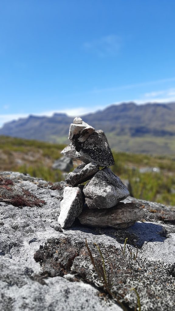 El Cocuy, a delicate stone balance sits atop a rock, set against a deep blue sky and towering mountains.