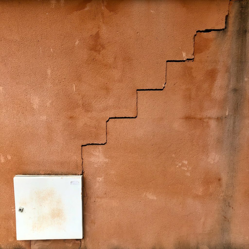A textured, reddish-tan wall with a prominent vertical crack that resembles the shape of stairs