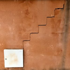 A textured, reddish-tan wall with a prominent vertical crack that resembles the shape of stairs
