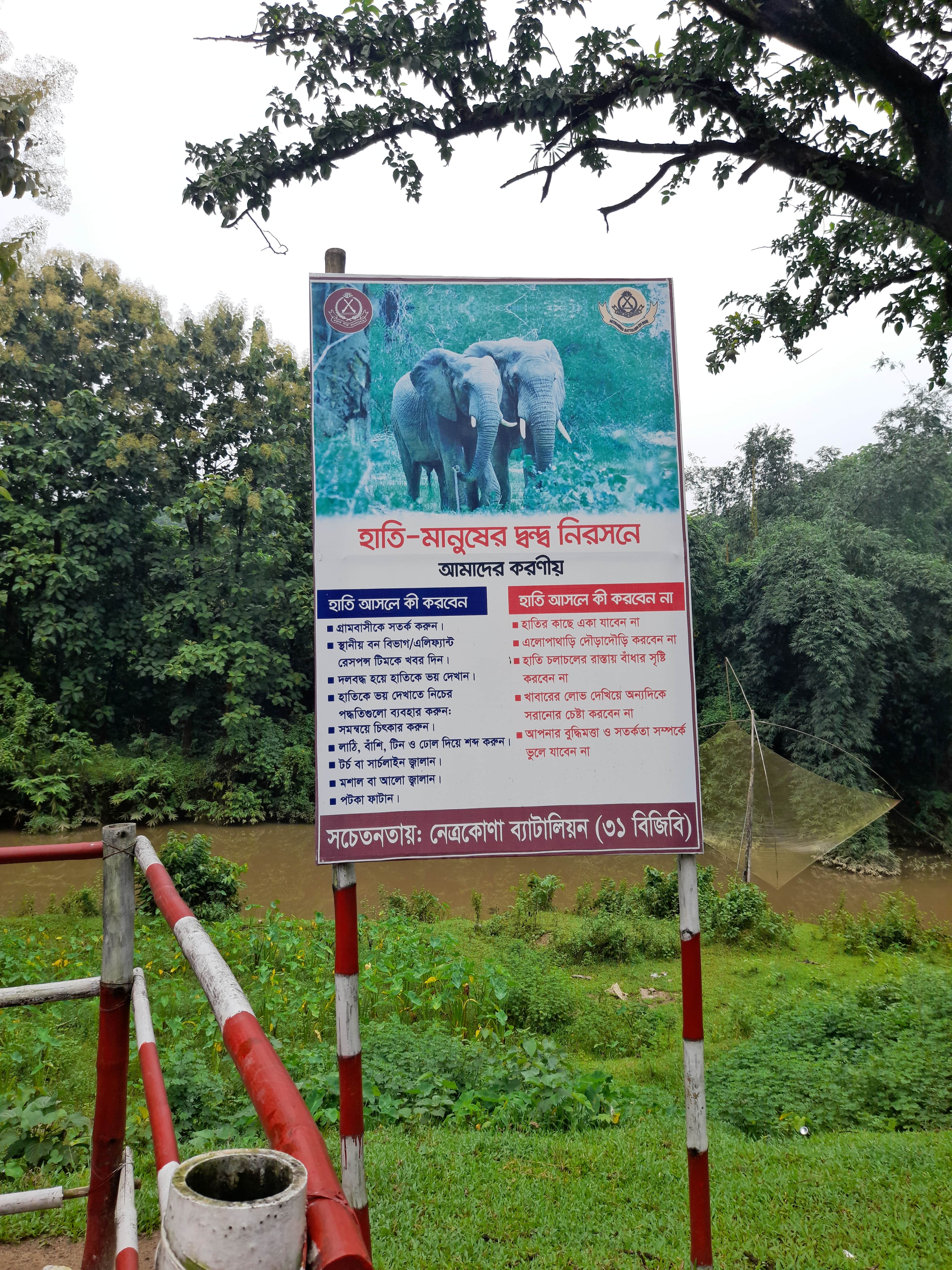 A sign attached to a fence near a river, indicating rules or safety information for visitors.