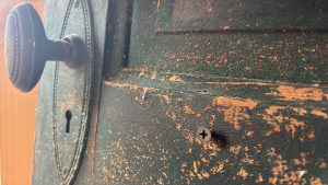 An old door, kind of close up, paint peeling.  The door knob is on the left, it's a vertical oval, set into a vertical oval knob plate.