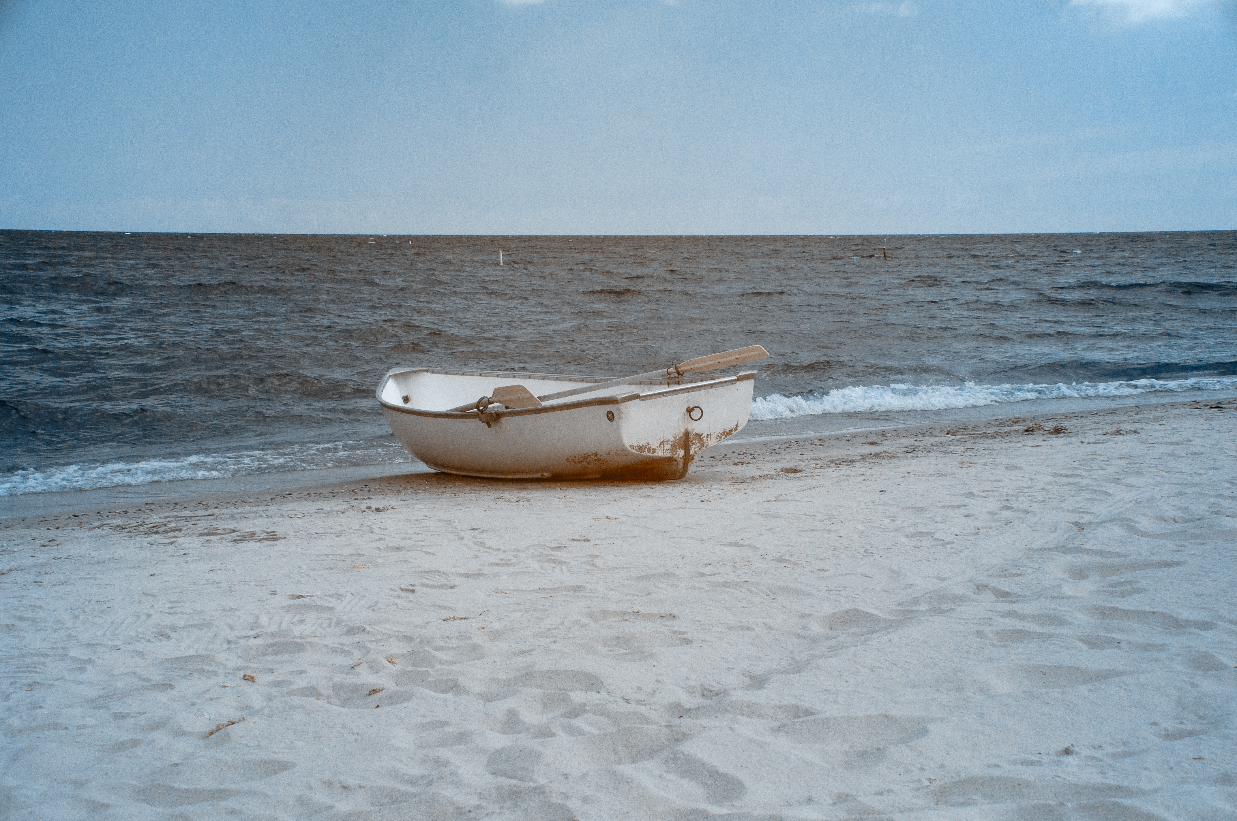 A row boat sits on a beach with light waves on the water and an endless horizon.