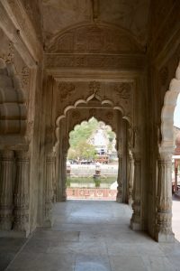 View through an arched marble doorway at Moosi Maharani Ki Chhatri (Alwar, Rajasthan) framing the pond and pavilions beyond.