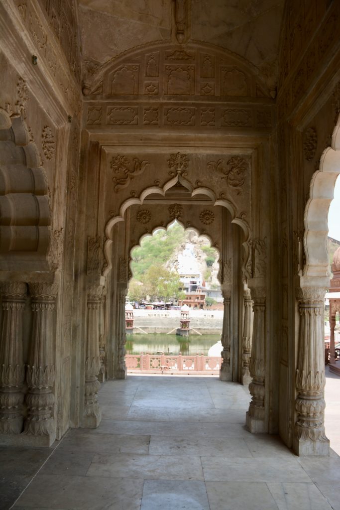 View through an arched marble doorway at Moosi Maharani Ki Chhatri (Alwar, Rajasthan) framing the pond and pavilions beyond.