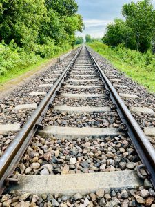 A perspective view of railway tracks extending into the distance, flanked by lush green foliage on either side

