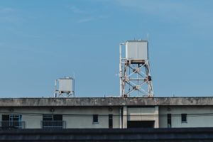 Water tanks on top of an aged residential building under a clear blue sky. A minimalist urban scene capturing everyday infrastructure, Japanese apartment life, and the contrast between structure and open sky
