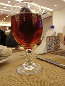 A glass of red wine in a wine glass, placed on a table with ceiling lights on its background.