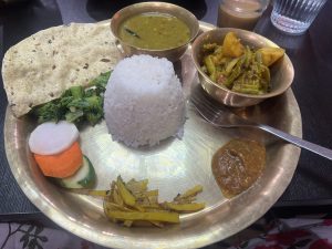 A traditional Nepali thakali thali with rice, dal (lentil soup), mixed vegetables, pickled vegetables, and a green salad, all served on a round brass plate.