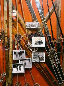 Glass display of vintage pairs of skis with attached vintage photos 