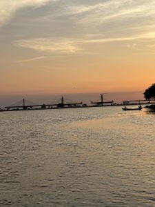 Evening sunset over the Holy Ganga River, with soft hues reflecting on the water and an unreconstructed bridge in view.