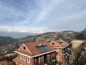 A view of a hillside village with buildings and terraced fields, seen from a balcony 