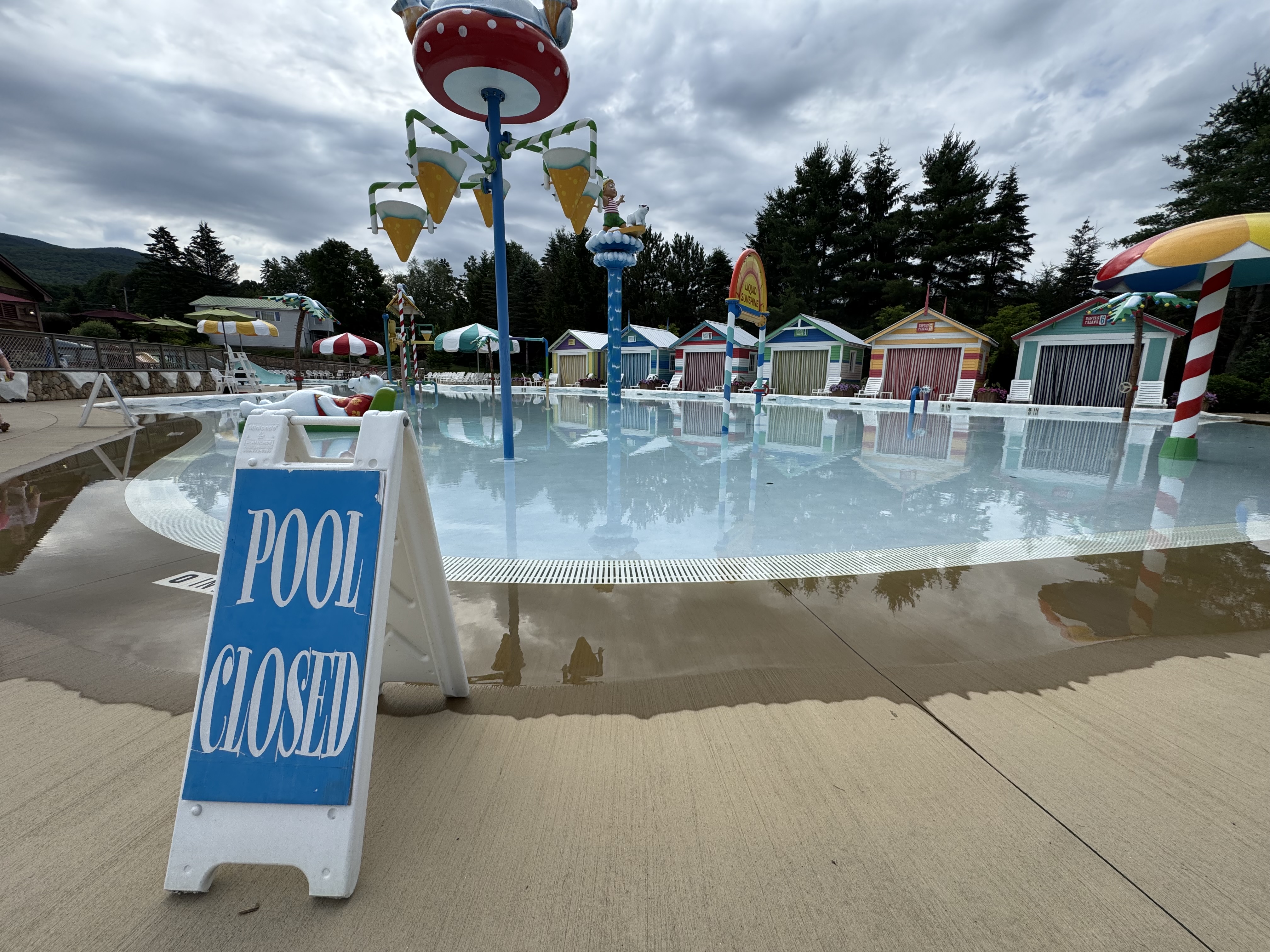 A splash pool surrounded by colorful cabanas and water features at Santa’s Village in Jefferson, New Hampshire. There’s a sign in the foreground that reads “pool closed.”