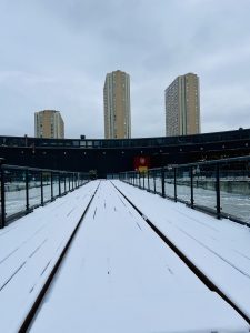 A snowy bridge in an outdoor stadium with tall apartment buildings in the background.